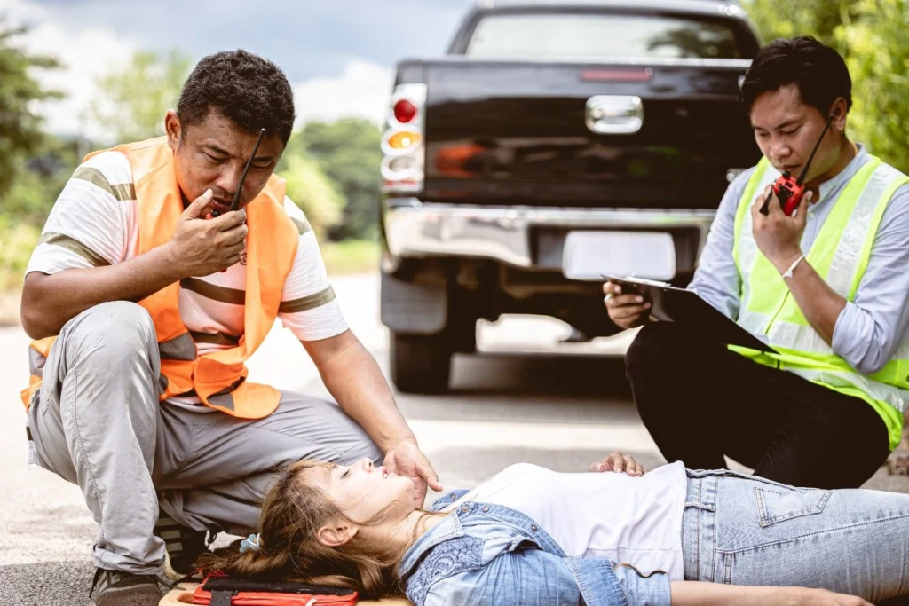 Injured worker on the ground beside a truck while a colleague in high-visibility clothing assists
